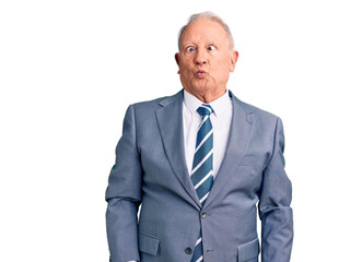 Senior handsome grey-haired man wearing elegant suit making fish face with lips, crazy and comical...