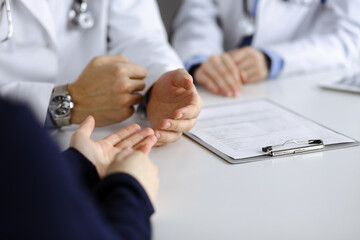 Unknown male doctor listening to his patient woman while sitting in modern clinic. Perfect medical service, medicine concept during Coronavirus pandemic. Covid 2019