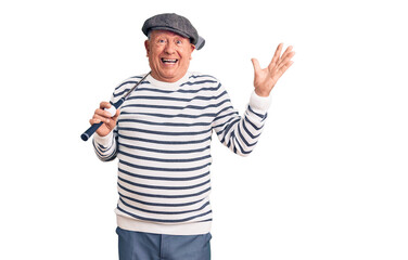 Senior handsome grey-haired man holding golf club and ball celebrating victory with happy smile and winner expression with raised hands