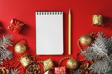 Notepad and pencil for writing wishes and gifts for the New Year and Christmas around the Christmas tree decorations on a red background.