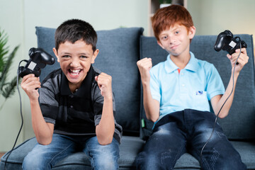 Point of view shot, Two kids cheering and shouting after won the online video game match while playing with joystick or gamepad at home sitting on sofa. © WESTOCK