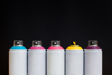 Five spray cans of graffiti paints on a black background: blue, pink, magenta, yellow and purple.