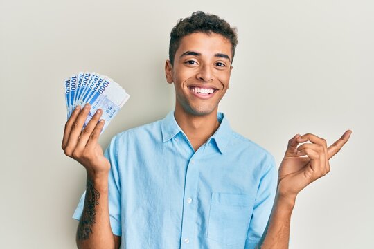 Young handsome african american man holding 1000 south korean won banknotes smiling happy pointing with hand and finger to the side