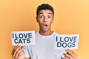 Young handsome african american man holding paper with i love cats and i love dogs phrase afraid...