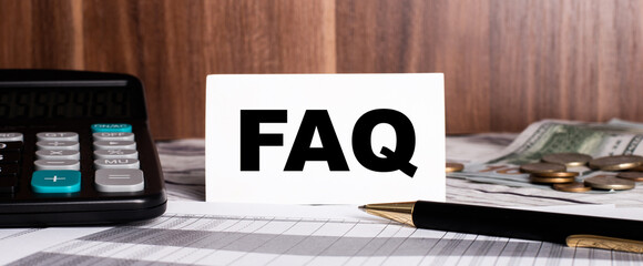 On a wooden background lies a pen with a calculator and a white card with the word FAQ