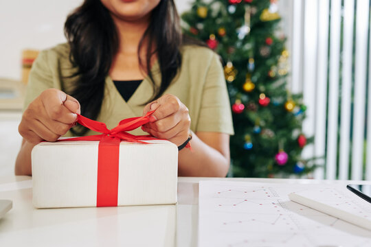 Close-up image of female entrepreneur opening Christmas present at office table