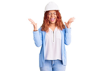 Young latin woman wearing architect hardhat celebrating mad and crazy for success with arms raised and closed eyes screaming excited. winner concept