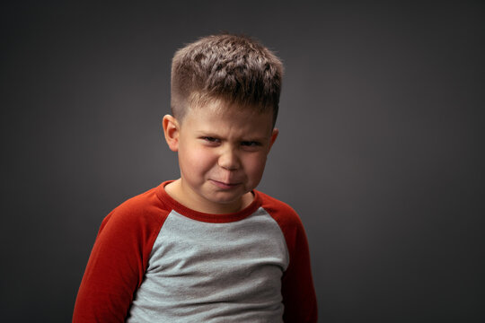 Angry boy frowning, showing with his face dislike isolated on grey background. Fake child emotions. Human emotions, facial expression concept. Facial expressions, emotions, feelings.