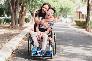Fototapeta na wymiar Mother and Asian Disabled child on wheelchair is playing, learning and exercise in the outdoor city park like other people with family,Life in the education age,Happy disability kid concept.