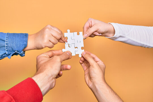 Hands of caucasian young people connecting pieces of puzzle over isolated yellow background