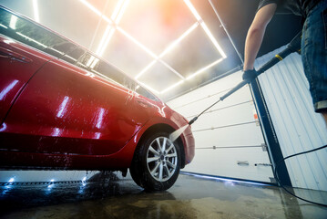 Worker washing car with high pressure water at a car wash.