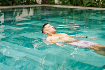 Handsome Asian man swimming in pool in the morning to get some refreshment on warm sunny day