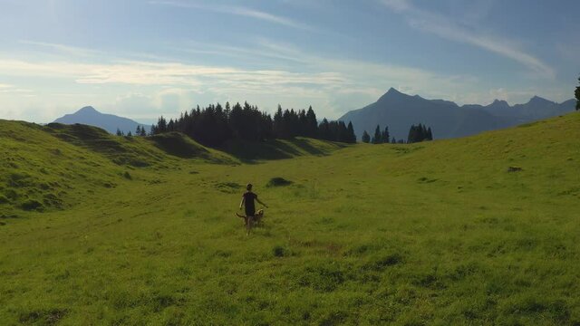 A beautiful young woman and her dog walk playfully into the distance on a vast plateau d'assy in the French, Alps