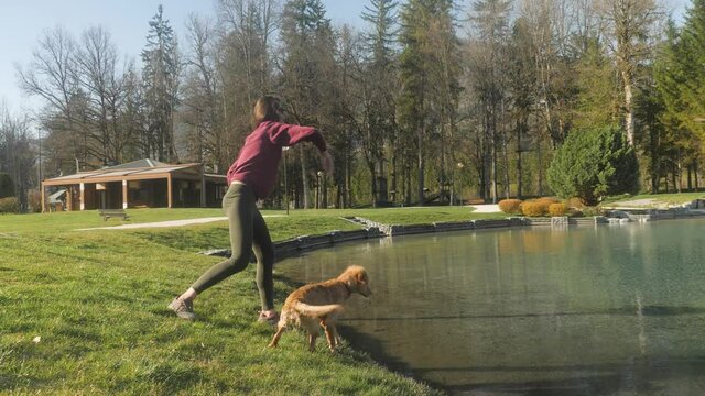 A gorgeous young woman tosses a ball in a mountain lake for her Golden Retriever puppy to fetch, in slow motion.
