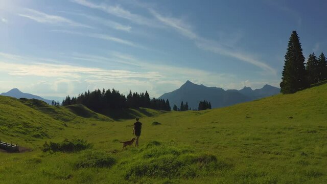 Frontward Travelling towards a beautiful young woman and her dog walk playfully into the distance on a vast plateau d'assy in the French, Alps