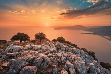 Moody sunset, the distant sun sets behind the silhouettes of blue mountains on the horizon, washed by the waters of the Mediterranean sea