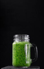 Green smoothie in the glass jar against the black background. Blended kale, apple, pear, orange juice and water. Healthy nutrition drink