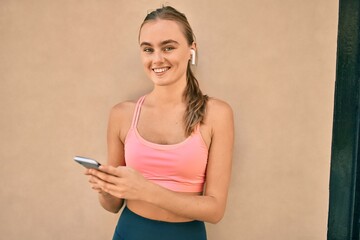Naklejka premium Young blonde sportswoman doing exercise using smartphone at the city.