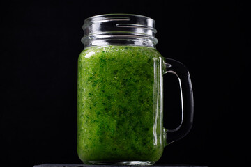 Green smoothie in the glass jar against the black background. Blended kale, apple, pear, orange juice and water. Healthy nutrition drink