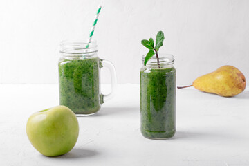 Green smoothie in the glass jars on the white table. Blended kale, apple, pear, orange juice and water. Healthy nutrition drink
