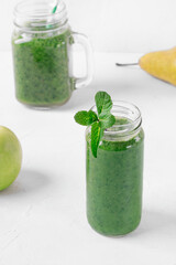 Green smoothie in the glass jars on the white table. Blended kale, apple, pear, orange juice and water. Healthy nutrition drink
