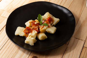 gourmet potato gnocchi with tomato sauce, parmesan and basil on black plate and wooden table