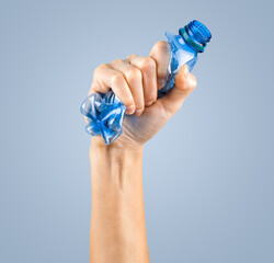 female hand squeezes an empty plastic bottle isolated on the blue. waste recycling concept