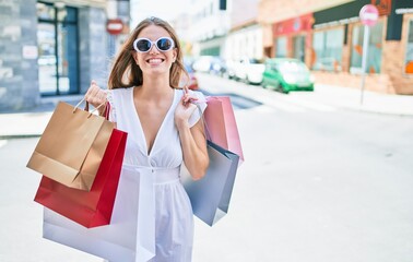 Young blonde woman smiling happy holding shopping bags at street of city