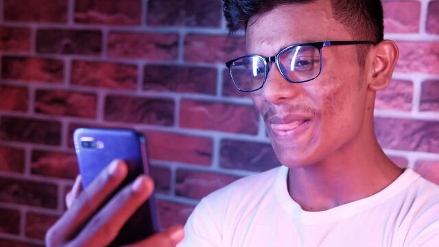 Smiling young man in glasses is using his phone to make a video call