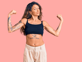 Fototapeta na wymiar Young hispanic woman with tattoo wearing casual clothes showing arms muscles smiling proud. fitness concept.