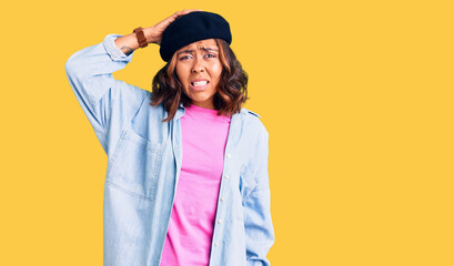 Young beautiful mixed race woman wearing french look with beret confuse and wonder about question. uncertain with doubt, thinking with hand on head. pensive concept.