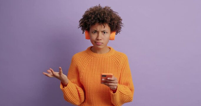Shocked puzzled woman being angry as app doesnt work tries to solve problem with mobile phone types something on display wears stereo headphones cannot understand what is wrong. Slow motion.