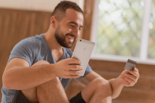 Low side shot of a cheerful man with smartphone and debit or credit card buying online equipment or doing sport bets and gambling online. Modern digital sports life. Sport app on smartphone. 