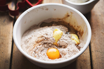 Gingerbread cookie ingredients in white bowl: eggs, spices, flour, egg