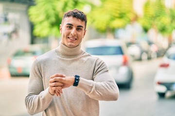 Young hispanic man smiling happy using watch at the city.