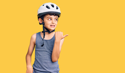 Little cute boy kid wearing bike helmet smiling with happy face looking and pointing to the side with thumb up.