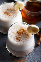 Banana smoothie with cinnamon in glasses with fruits on stone background.