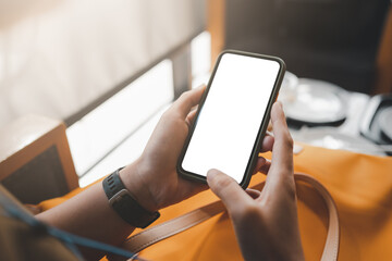 Hand holding Mockup mobile phone with blank white screen in cafe or coffee shop. A blank phone...