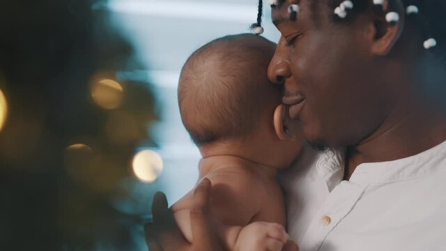 Close up, newborn baby and father cuddling in front of the christmas tree with golden lights. High quality 4k footage