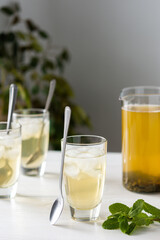 Cold refreshing green tea with ice and mint, tea jug and glasses on white wooden background