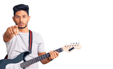 Handsome latin american young man playing electric guitar pointing with finger to the camera and to you, confident gesture looking serious