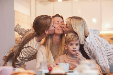 Obraz na płótnie Canvas Portrait of happy mother enjoying kisses from three children while sitting at breakfast table in kitchen