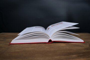 open paper book with red cover lies on a wooden table closeup, hand flipping pages, reading concept, copy space