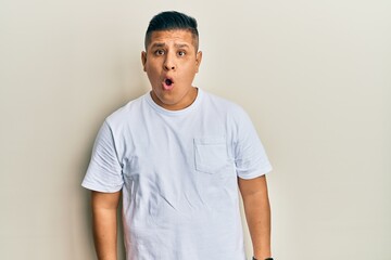 Young latin man wearing casual white t shirt afraid and shocked with surprise expression, fear and excited face.