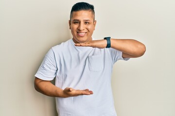 Young latin man wearing casual white t shirt gesturing with hands showing big and large size sign, measure symbol. smiling looking at the camera. measuring concept.