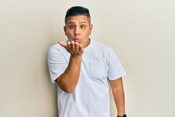 Young latin man wearing casual white t shirt looking at the camera blowing a kiss with hand on air being lovely and sexy. love expression.