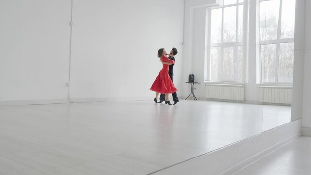 Young beautiful couple studying ballroom dance. A professional ballroom dancing couple dances in a large, bright, white hall
