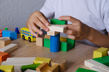 kid, boy builds towers and buildings from colored wooden figures, concept of housing construction, mortgage, insurance, happy childhood, children's games