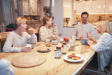 Wide angle portrait of big happy family enjoying breakfast together sitting at table in kitchen , focus on smiling father and three kids, copy space - Powered by Adobe