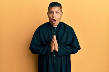 Obraz premium Young latin priest man praying with hands together afraid and shocked with surprise and amazed expression, fear and excited face.